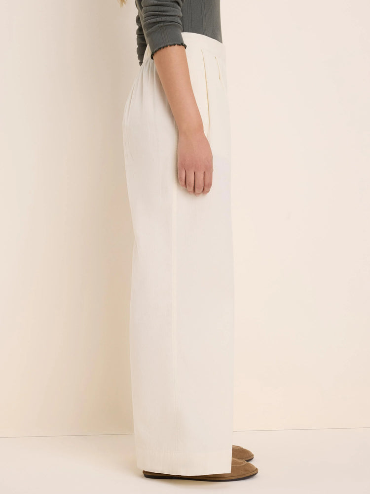 Cream baby cord wide-leg pants with front pleats, shown from the side on a model.