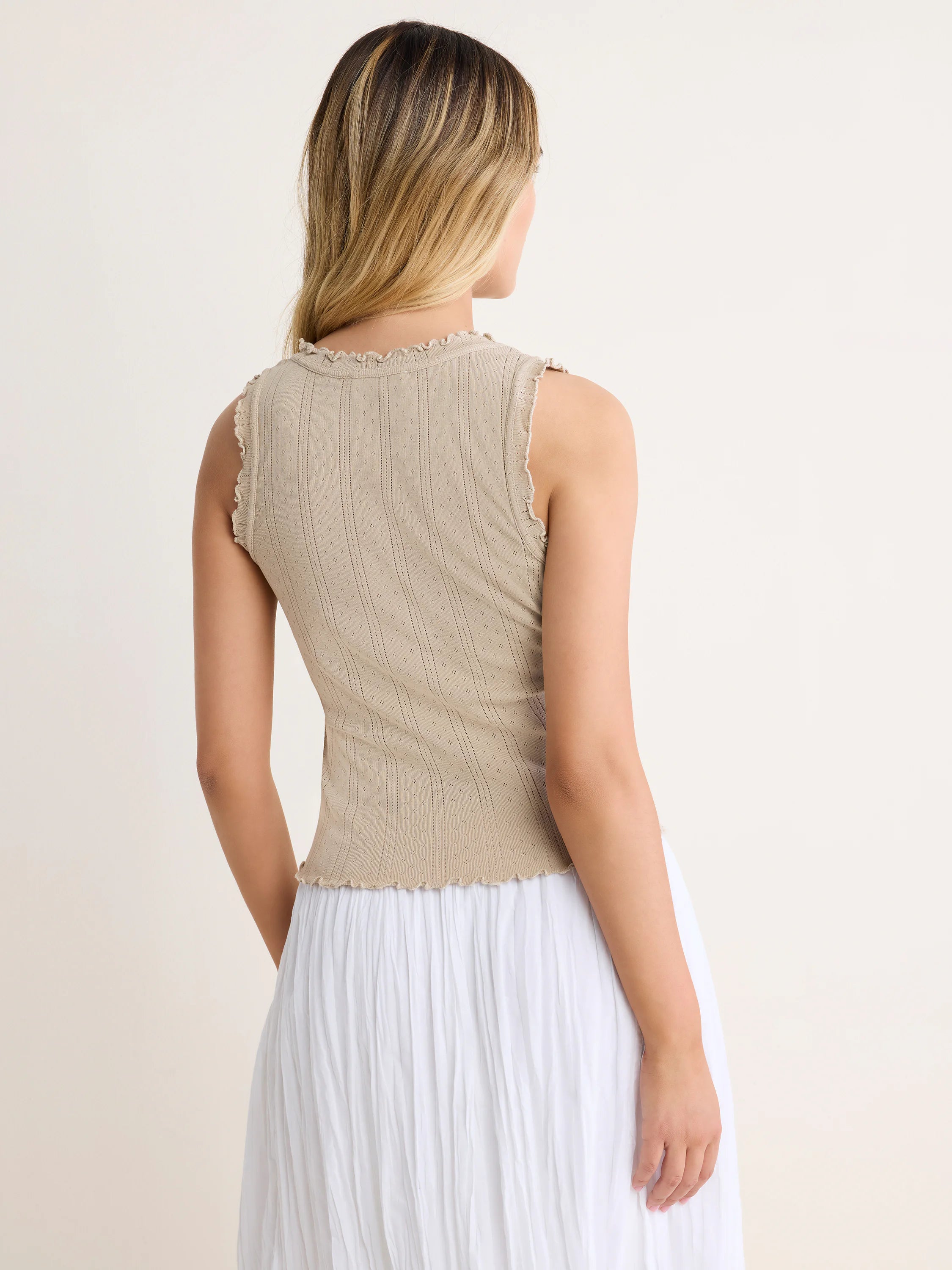 Light tan pointelle rib tank with ruffled neckline, armholes, and wavy hem. Model shown from the back.