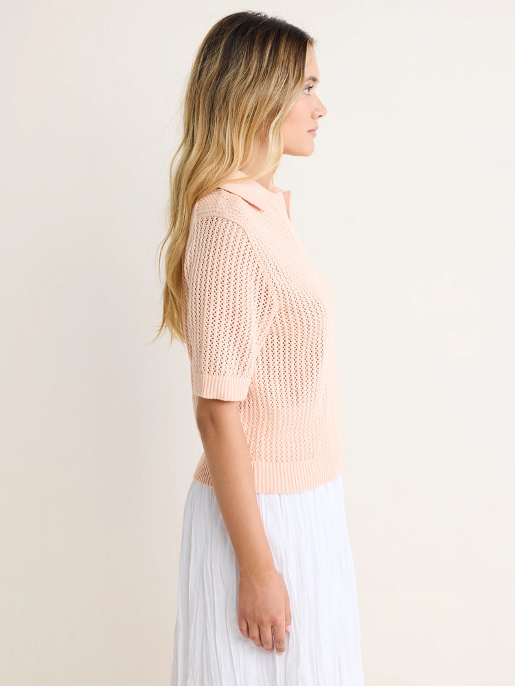 Blush pink mesh polo sweater with short sleeves and ribbed hem, shown on a model in profile.