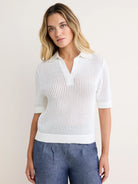 White mesh polo sweater with polo collar, V-neck, short sleeves, and ribbed trim. Worn with blue pants.