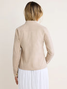Back view of a light beige cotton twill jacket. It has a stand collar, shoulder yoke, vertical back seams, and button cuffs.