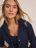 Navy blue collared cotton shirt, crinkled texture, silver snap buttons, worn open over a dark top.