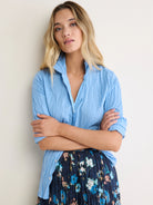 Light blue crinkled cotton shirt with a relaxed open collar, rolled-up sleeves, and silver snap buttons on the side.