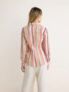 Crinkled shirt with vertical stripes in tan, light pink, white, and black. Model wears from back.
