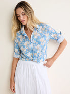 Light blue shirt with cream floral pattern, rolled sleeves, tied at waist. Crinkled fabric.