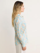 Crinkled cotton shirt with light blue floral shapes on a beige background. Long sleeves and collared.