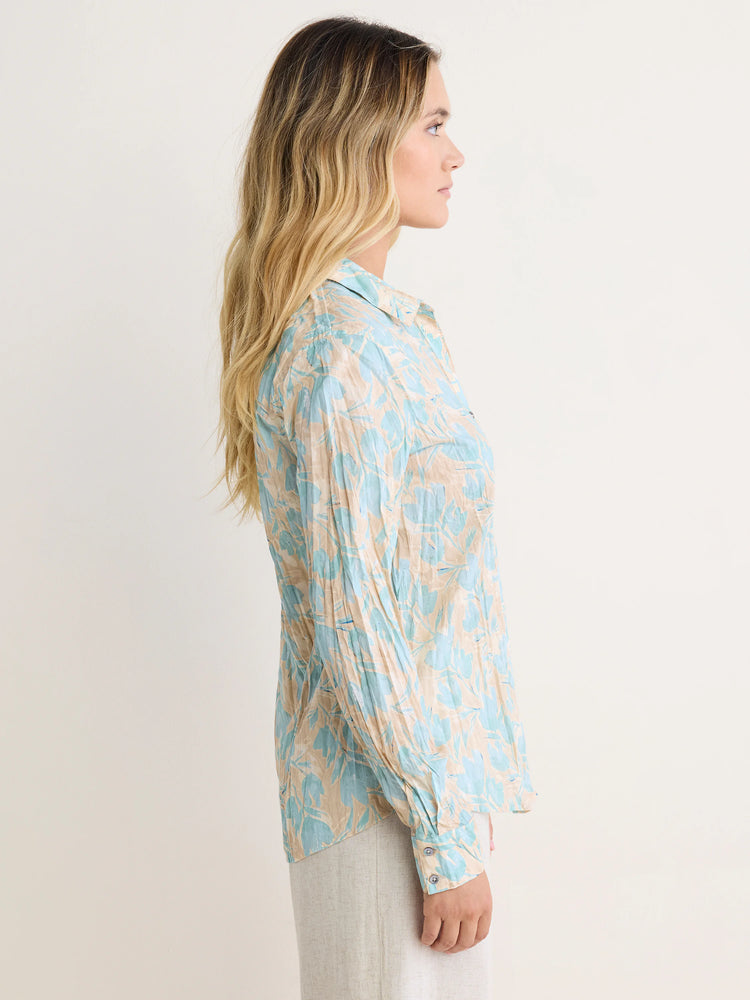 Crinkled cotton shirt with light blue floral shapes on a beige background. Long sleeves and collared.