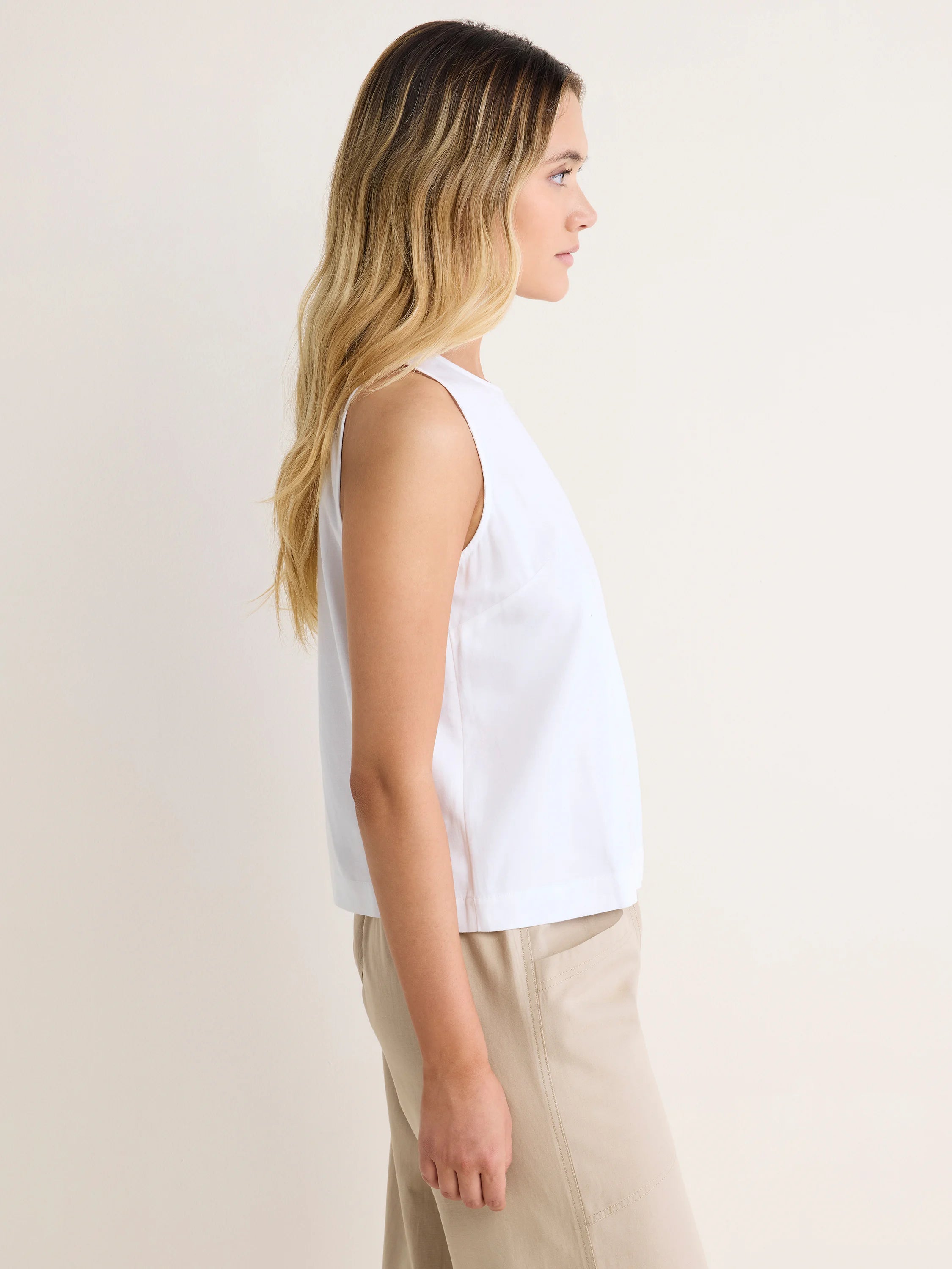 White sleeveless tank top with a high neck and relaxed fit, shown on a model in profile.