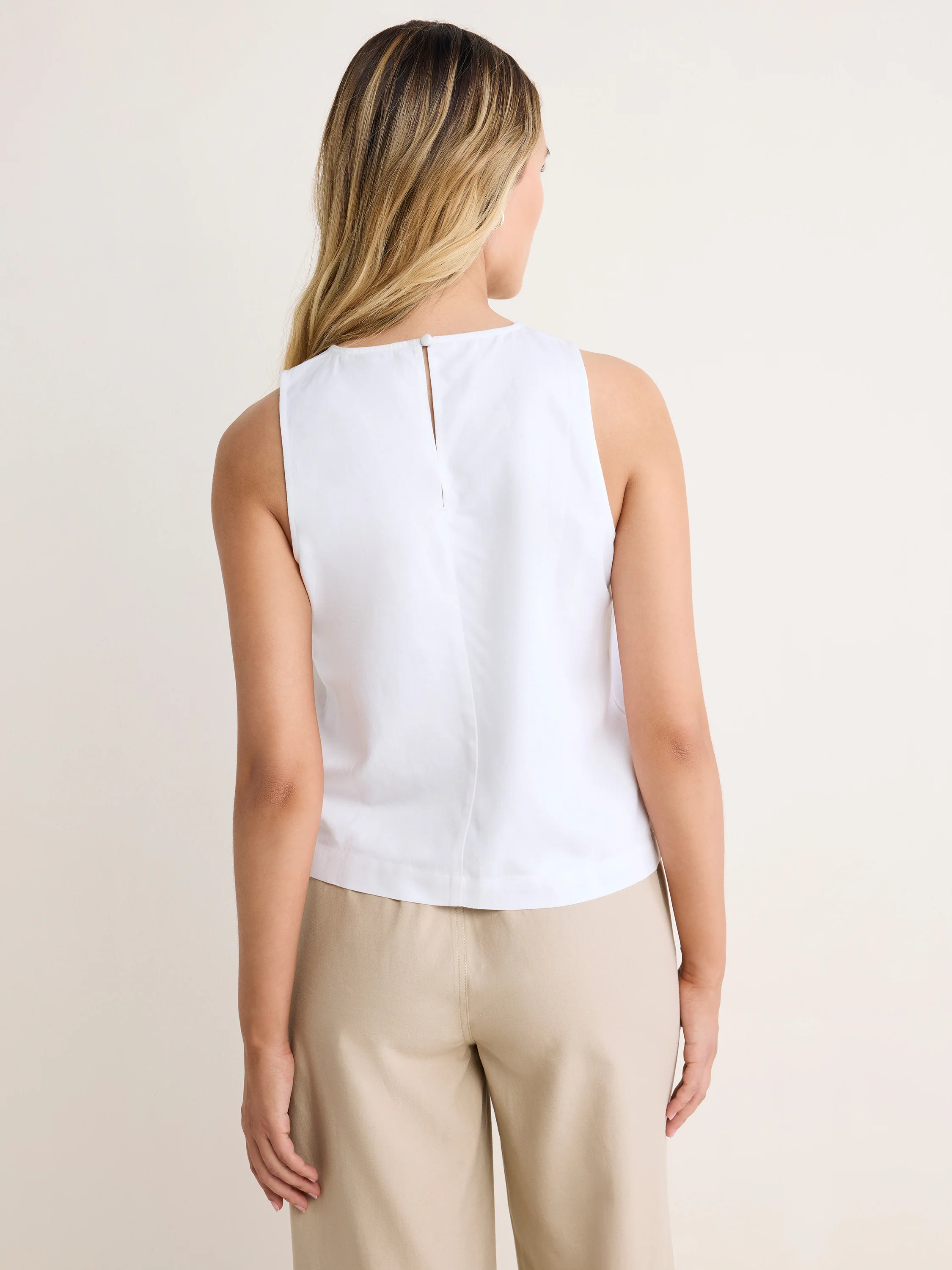 White sleeveless tank with a keyhole and button closure at the back, featuring a relaxed fit.