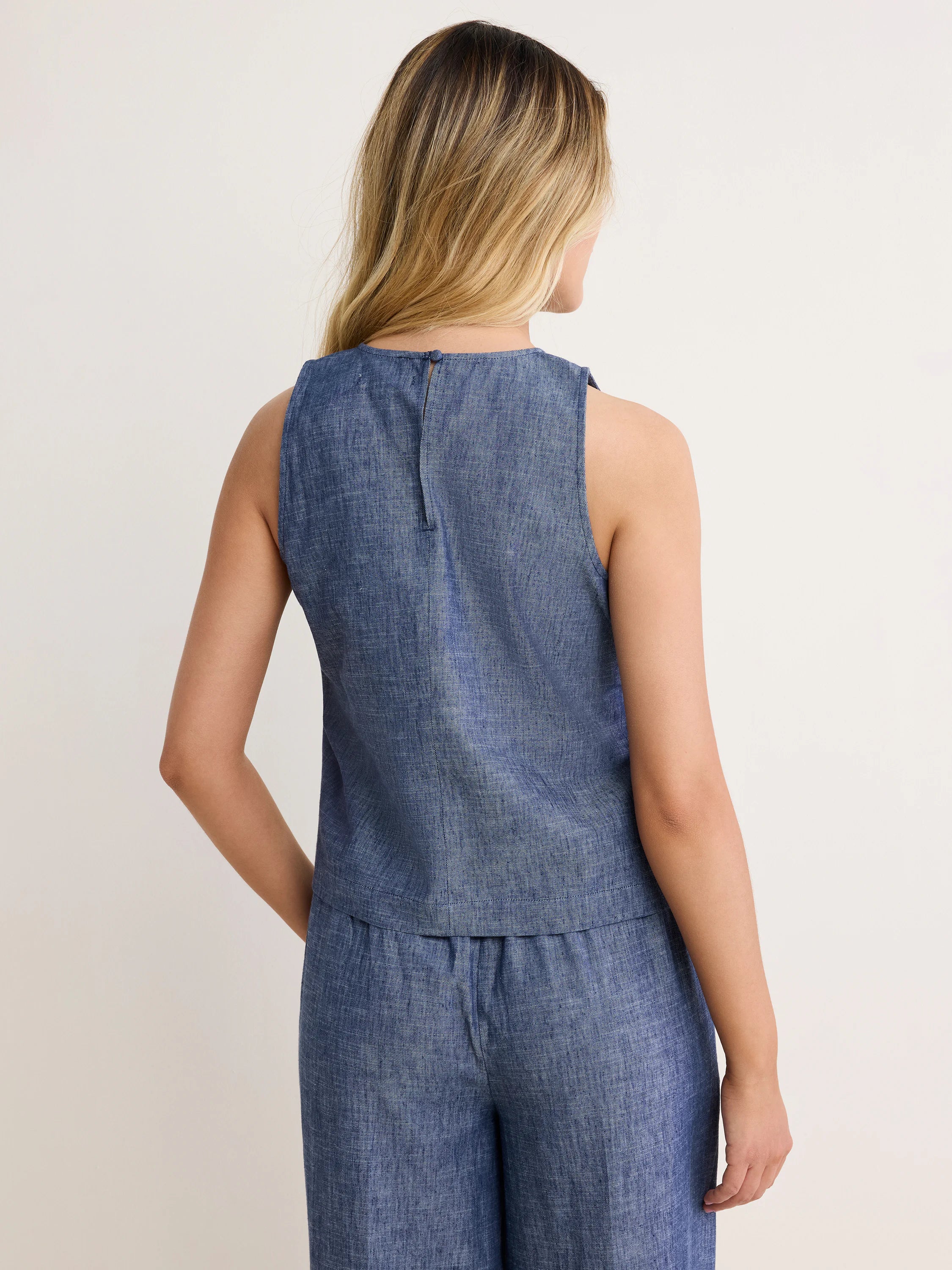 Back view: Blue chambray sleeveless tank with a round neck, keyhole & button closure, and visible slub texture.
