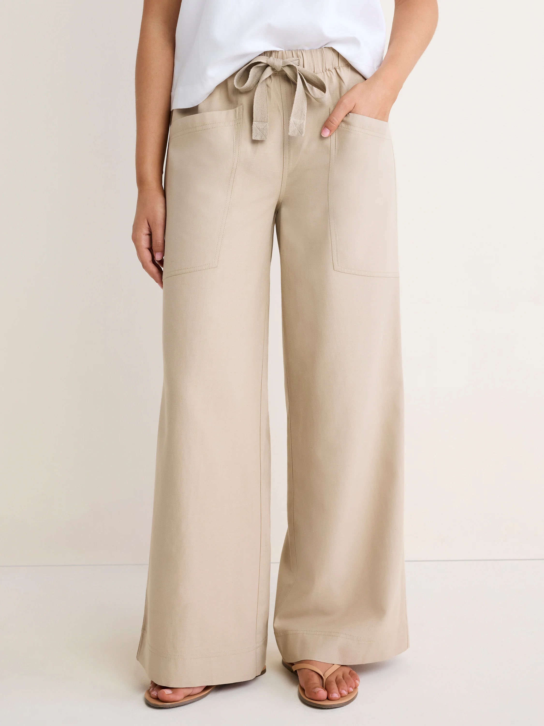 Beige wide-leg pants with elastic waist, drawstring tie, and two large front patch pockets.