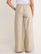 Light beige wide-leg cotton linen pants, high-waisted with a gathered elastic waistband, shown on a model from the back.