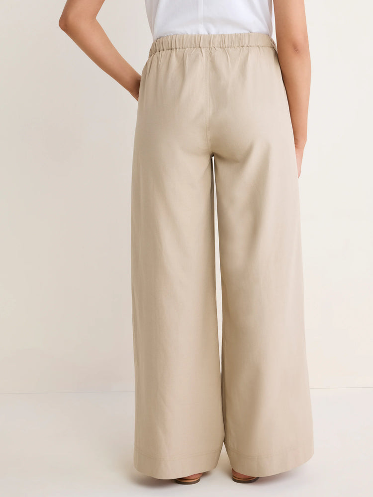 Light beige wide-leg cotton linen pants, high-waisted with a gathered elastic waistband, shown on a model from the back.