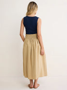 Navy sleeveless dress with a tan crinkled midi skirt and gathered elastic waist. Model from back.