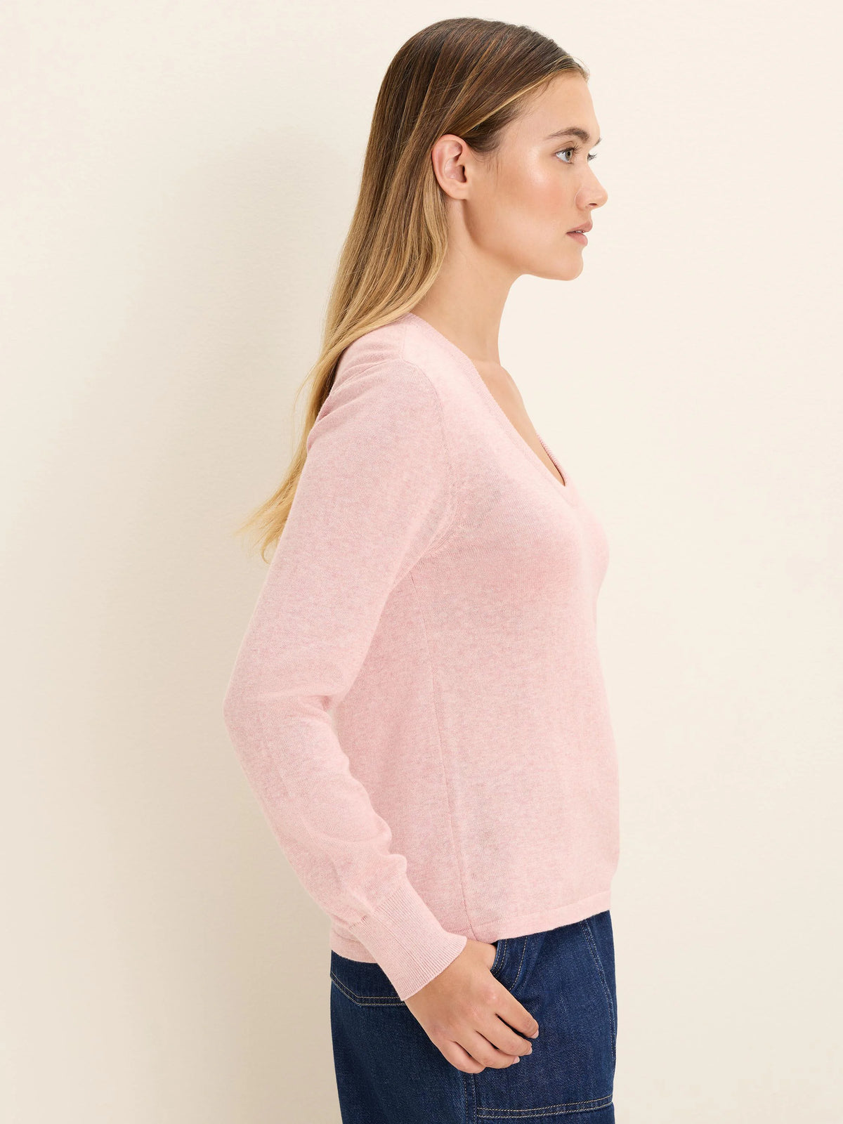 Light pink, fine-knit V-neck sweater with long sleeves on a model, seen from the side.