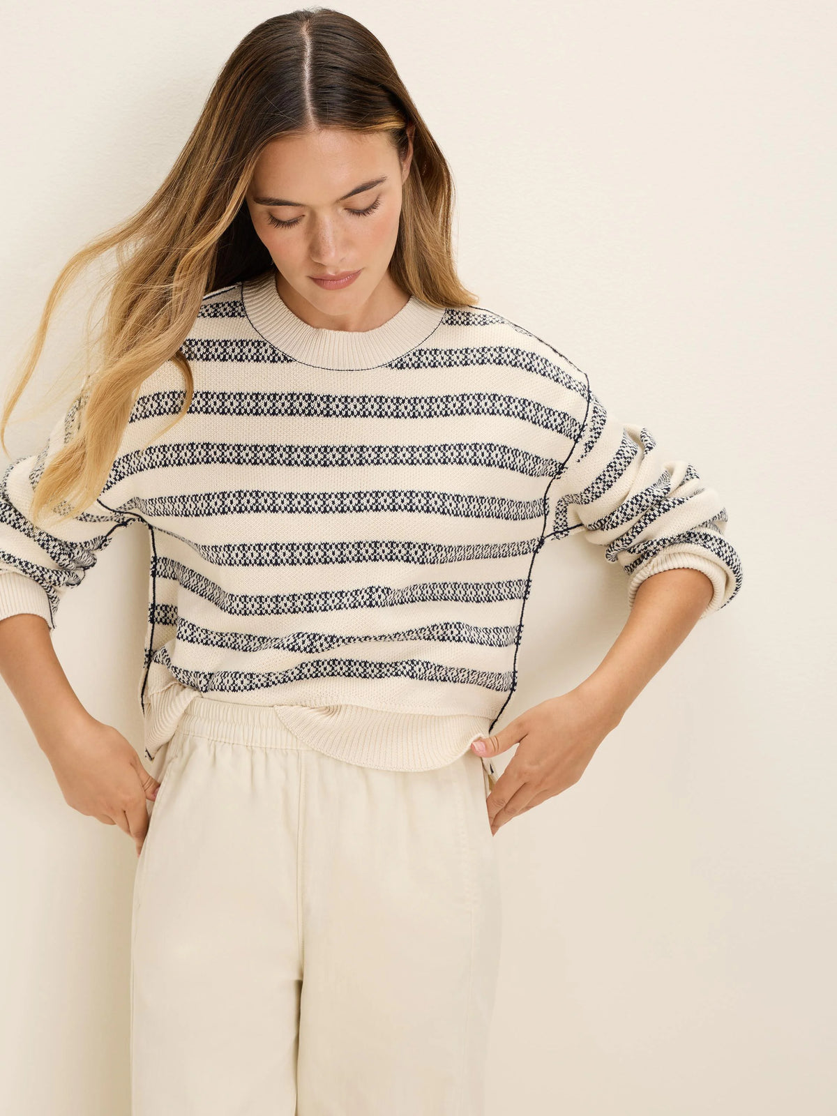 Ecru knit sweater with dark blue horizontal geometric jacquard stripes and contrast stitching.