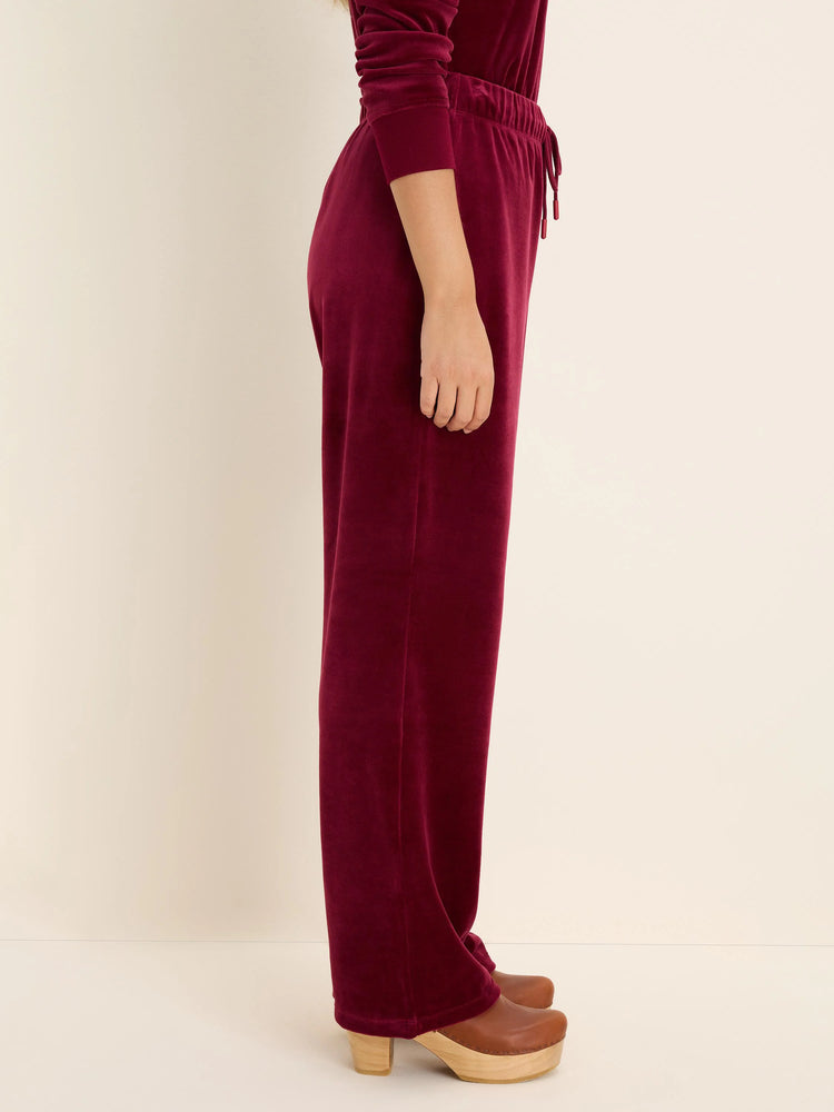 Burgundy velour pants with an elastic drawstring waist and wide legs, worn by a model.