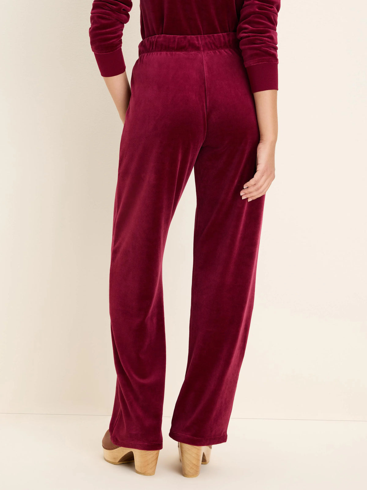 Burgundy velour pants with an elasticated waist and straight legs, worn by a model facing away.