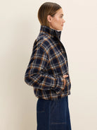 Plaid jacket in navy, brown, and cream. Features a high collar, zippered front, and cinched hem, worn by a model.