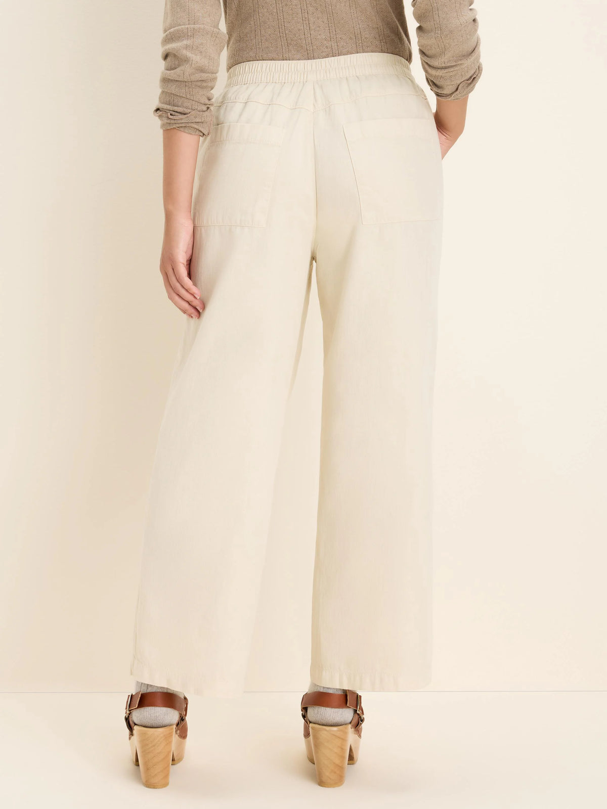 Rear view of cream wide-leg denim ankle pants with an elastic waist and back patch pockets.