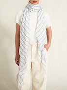 White scarf with light grey diagonal stripes and frayed edges.