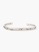 Gold cuff bracelet with row of small, light purple and gray stones.