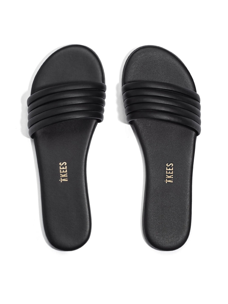 Black leather slides with three horizontal bands across the top.  "TKEES" is embossed on the soles in gold.