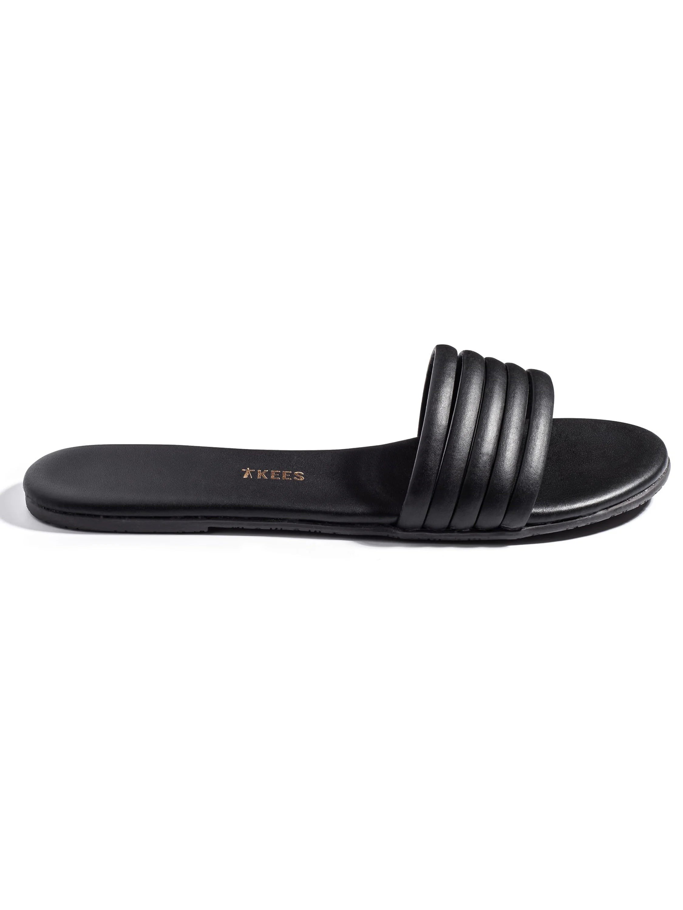 Black leather slide sandal with a padded, ribbed strap.  Sole is also black.  Tkees logo is subtly embossed.