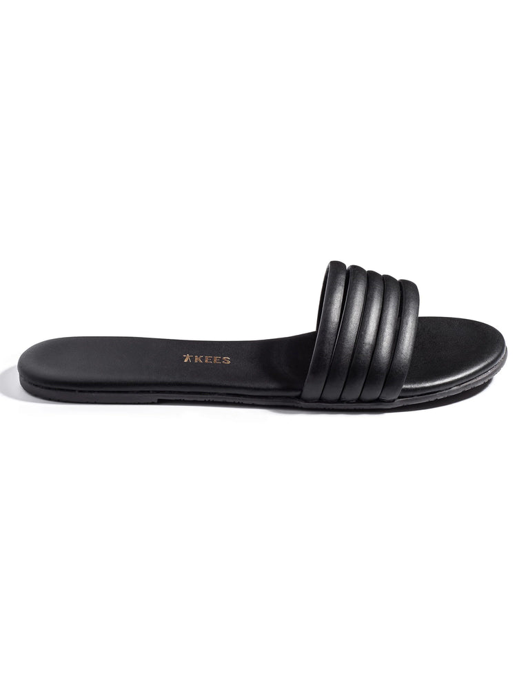 Black leather slide sandal with a padded, ribbed strap.  Sole is also black.  Tkees logo is subtly embossed.
