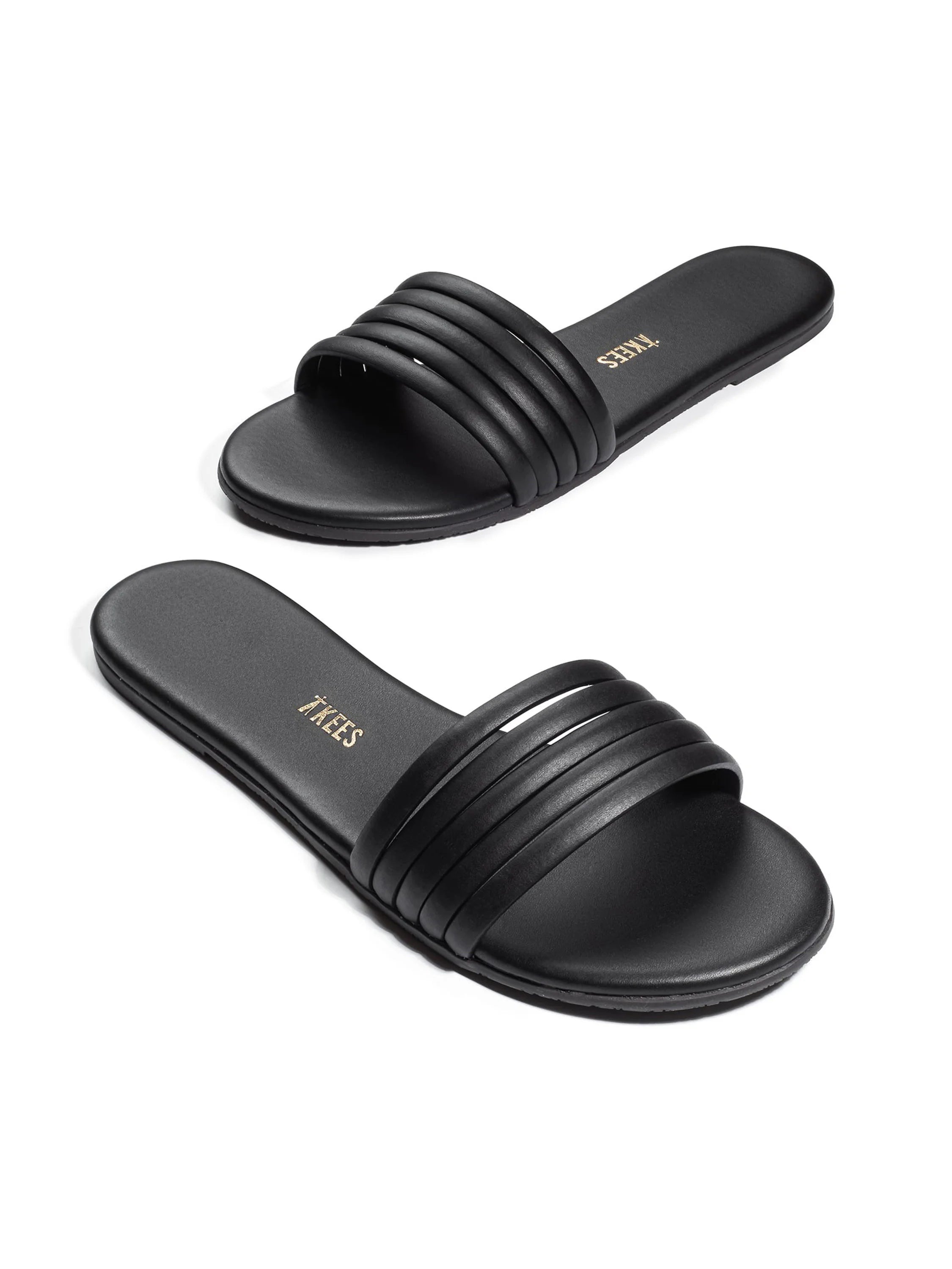Black leather slide sandals with five parallel straps across the vamp.  The Tkees logo is visible on the insole.
