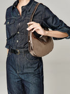 Small metallic bronze crescent shoulder bag, worn on a model's shoulder against a dark denim outfit.