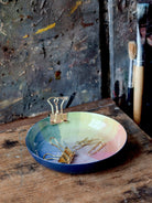 Round enamel tray; navy blue rim, pastel rainbow interior.  Gold binder clips inside.