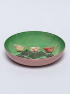 Round tray with pink exterior and green interior. Inside, three stylized flowers (striped, checkered, solid orange/red)...
