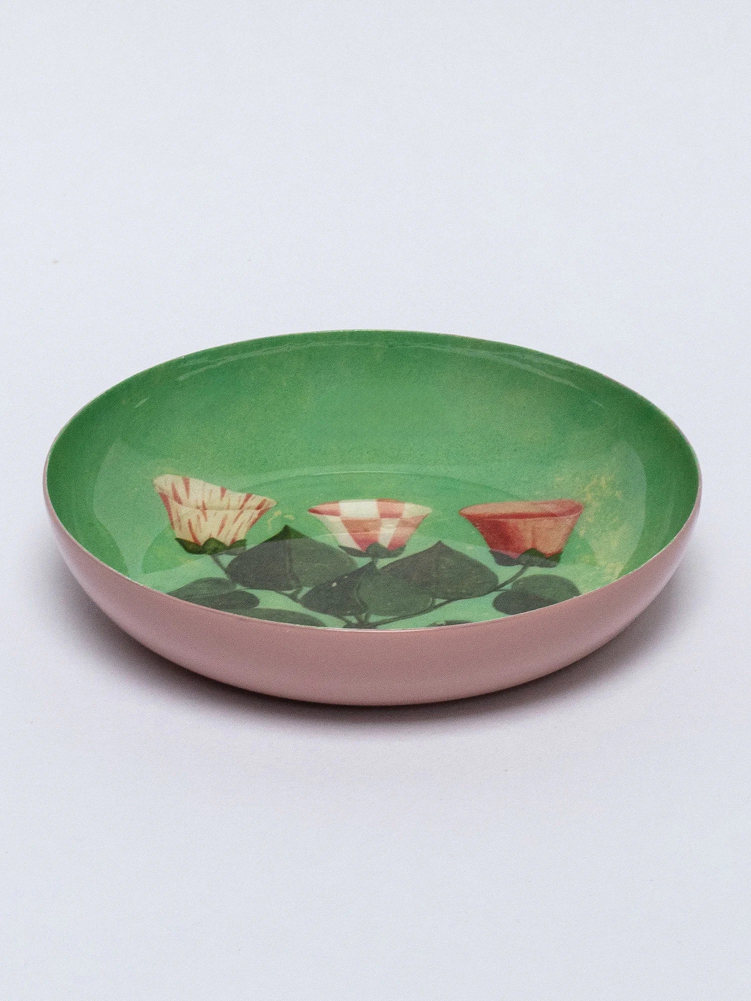 Round tray with pink exterior and green interior. Inside, three stylized flowers (striped, checkered, solid orange/red)...