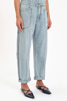 Light wash blue barrel leg jeans with tied drawstring, large front patch pockets, exposed vertical seams, shown cuffed.