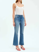 High-waisted, medium-wash blue, flared jeans with a raw hem.  Model also wears a white ribbed tank top and red shoes.