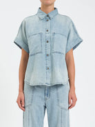 Light blue denim top with collar, button front, two chest pockets, and rolled short sleeves.