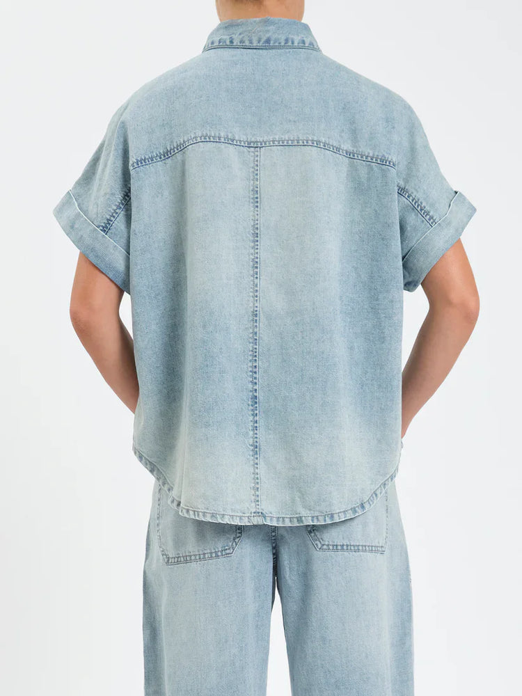 Faded light blue denim top, back view. Rolled short sleeves, back yoke, rounded hem.