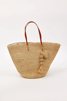 Tapered natural straw tote bag with brown leather handles. Features straw balls, tassel, and heart charms.