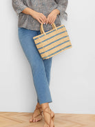 Rectangular woven straw bag, natural beige with horizontal muted blue stripes. Short straw handles.