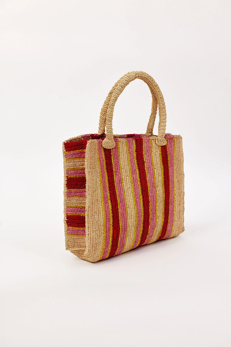 Woven raffia tote bag with vertical stripes in tan, red, pink, and yellow. Features braided handles.