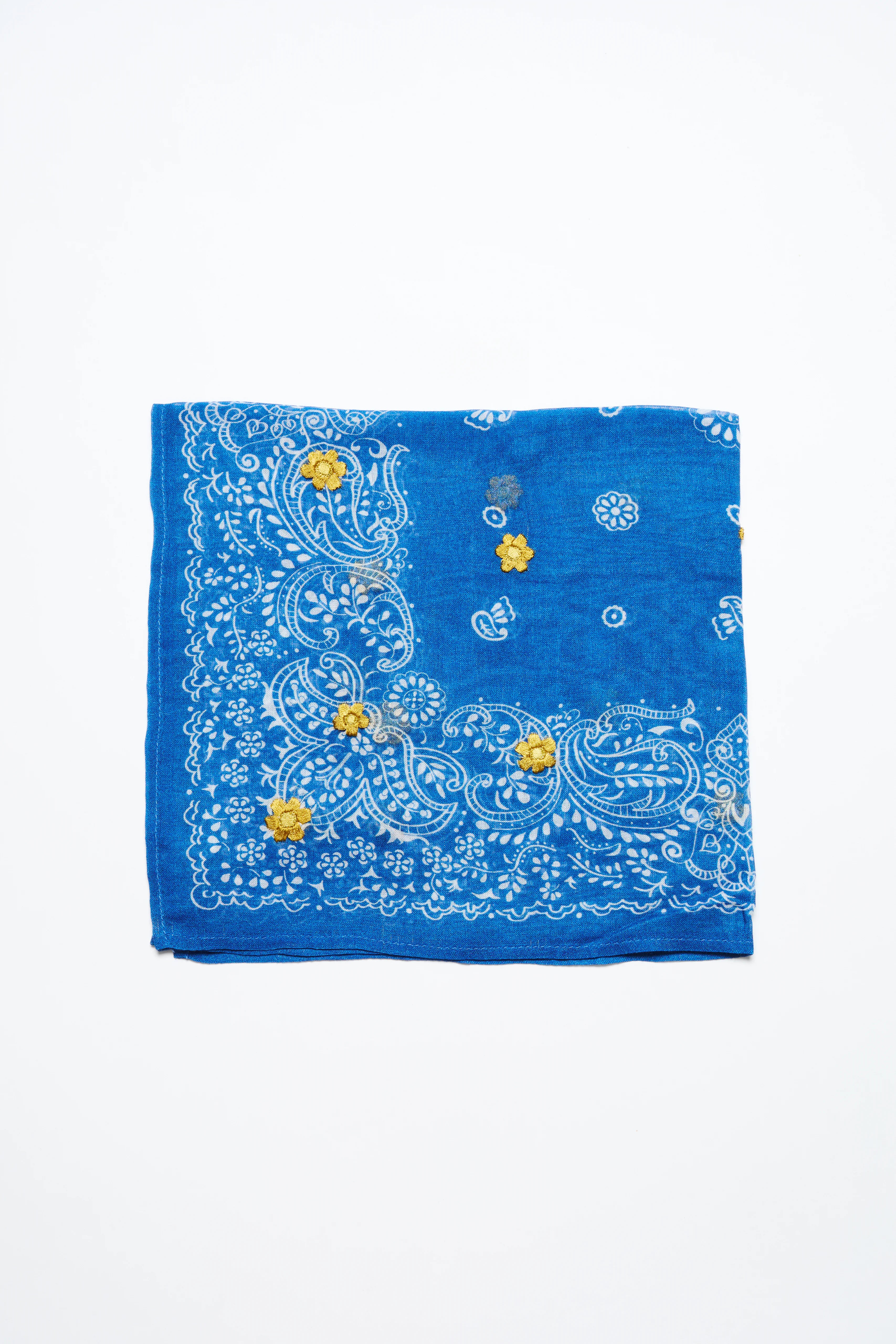 Folded blue bandana with white paisley print and yellow embroidered flowers.