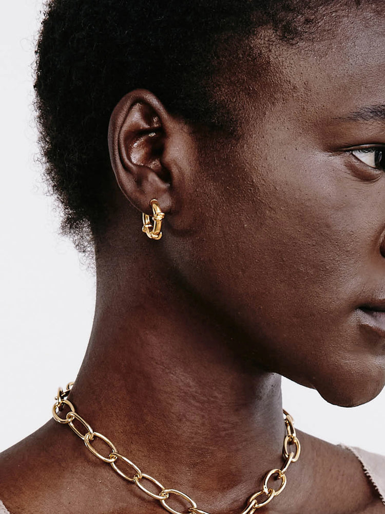 Small gold hoop earrings with a wrapped, shiny finish, worn on an ear.