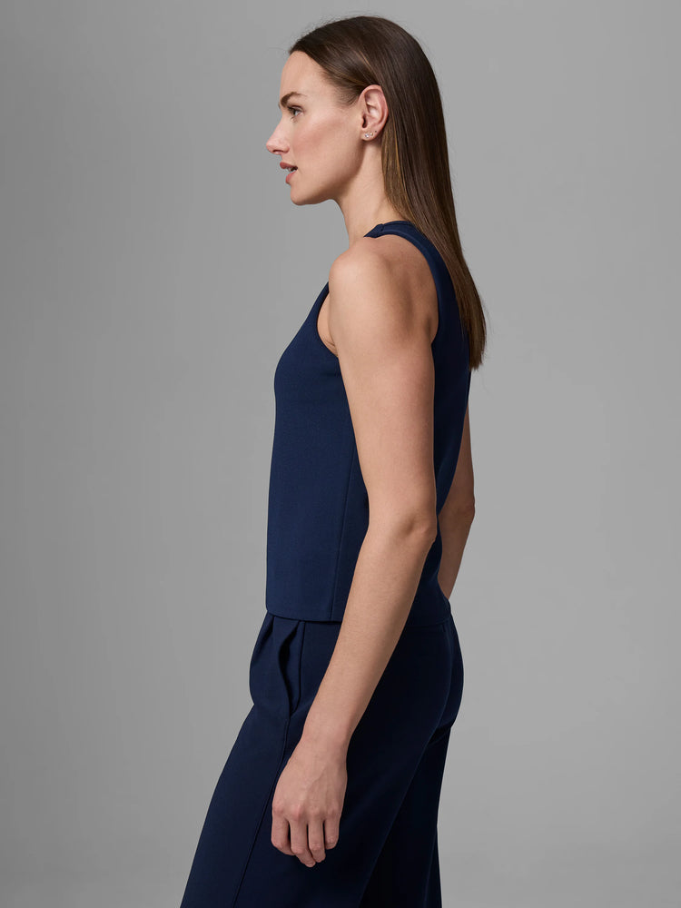 Navy knit scuba tank, sleeveless with a high, round neck, worn by a woman in side profile.