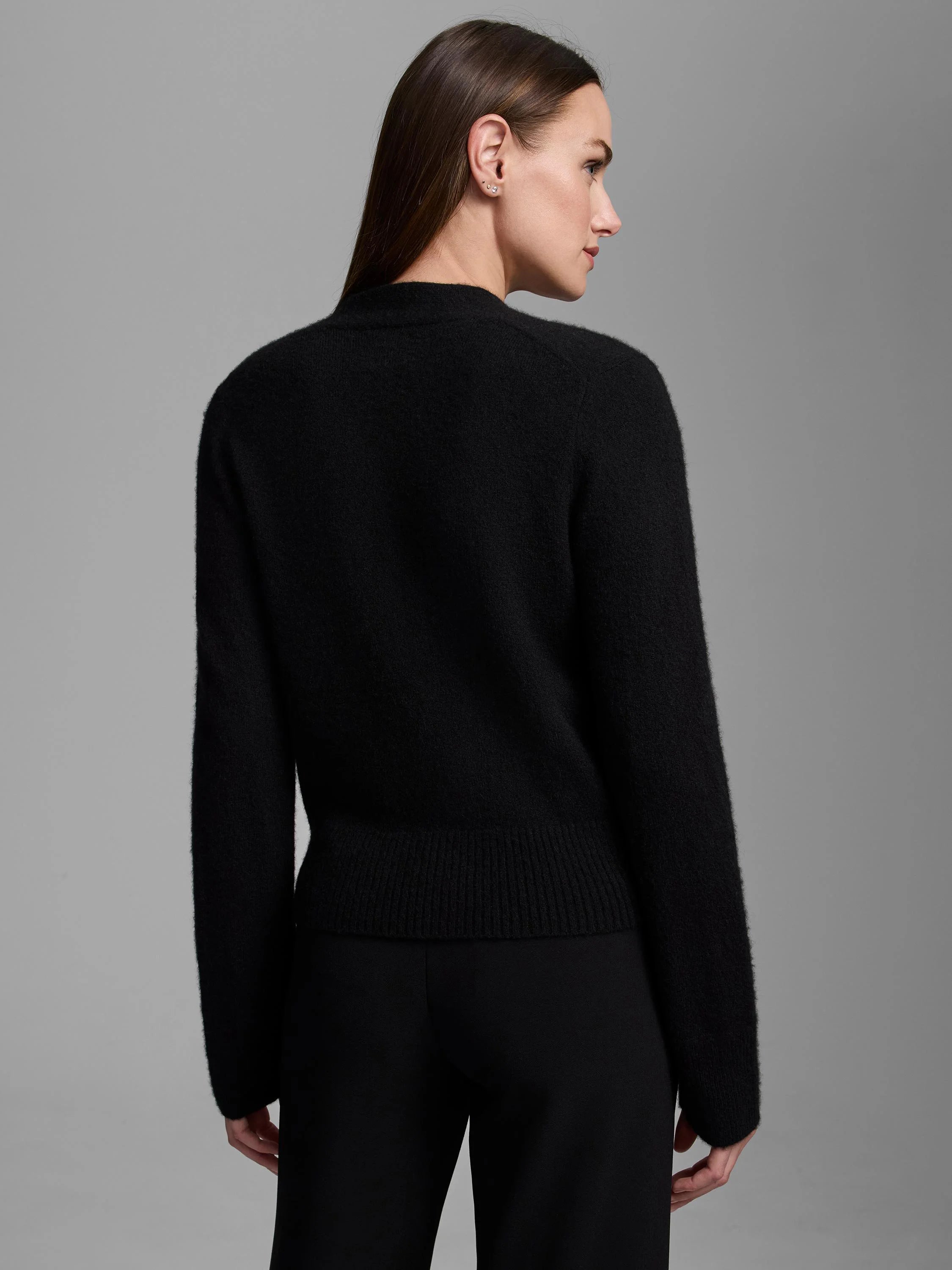 Black cashmere cardigan, back view on model. Long sleeves, soft textured knit, ribbed bottom hem.