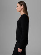 Black cashmere V-neck sweater with a relaxed fit and long sleeves, featuring a side slit, worn by a woman from the side.