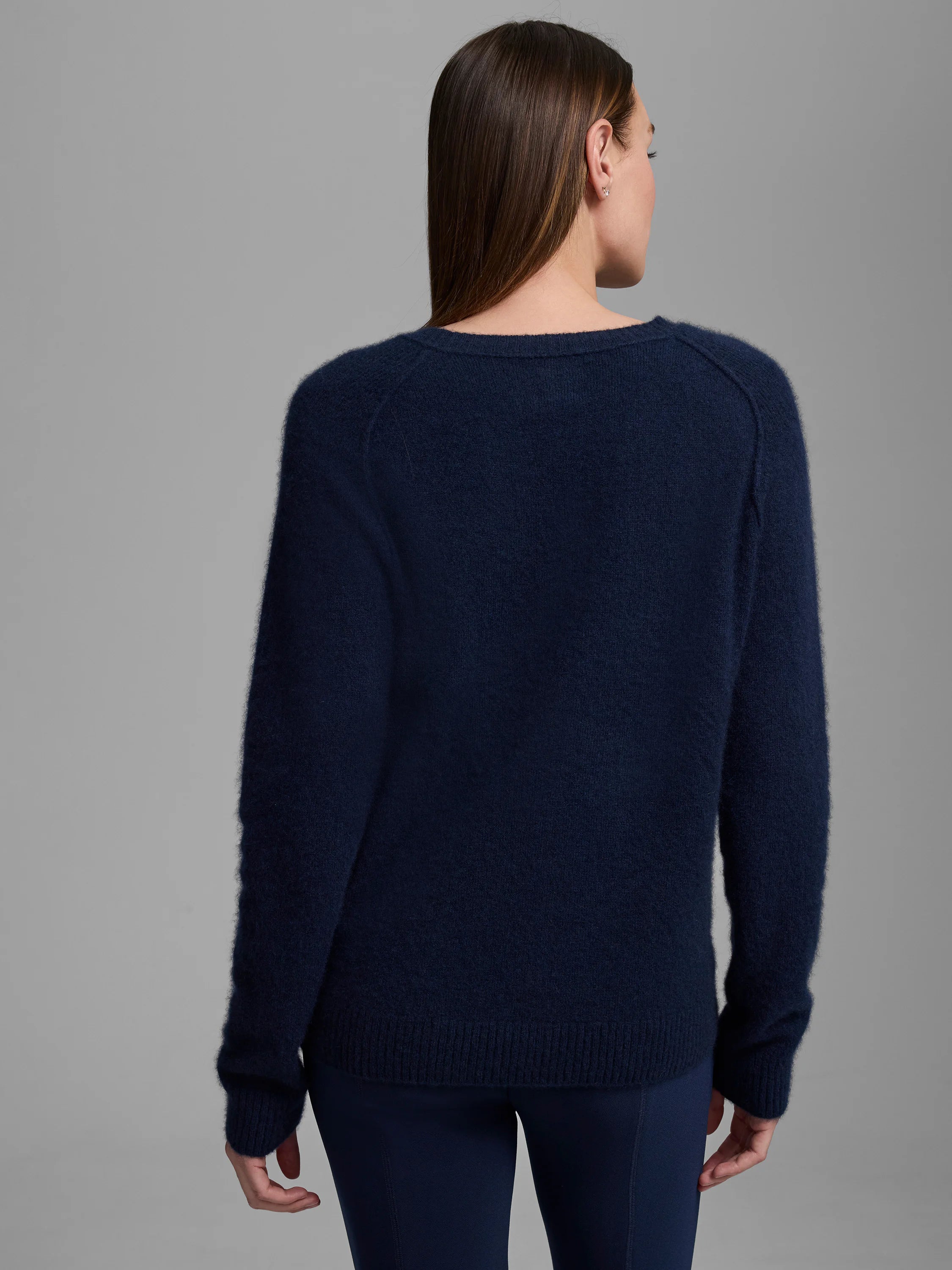 Rear view of a model in a navy blue fuzzy sweater with a crew neck, long raglan sleeves, and ribbed cuffs/hem.