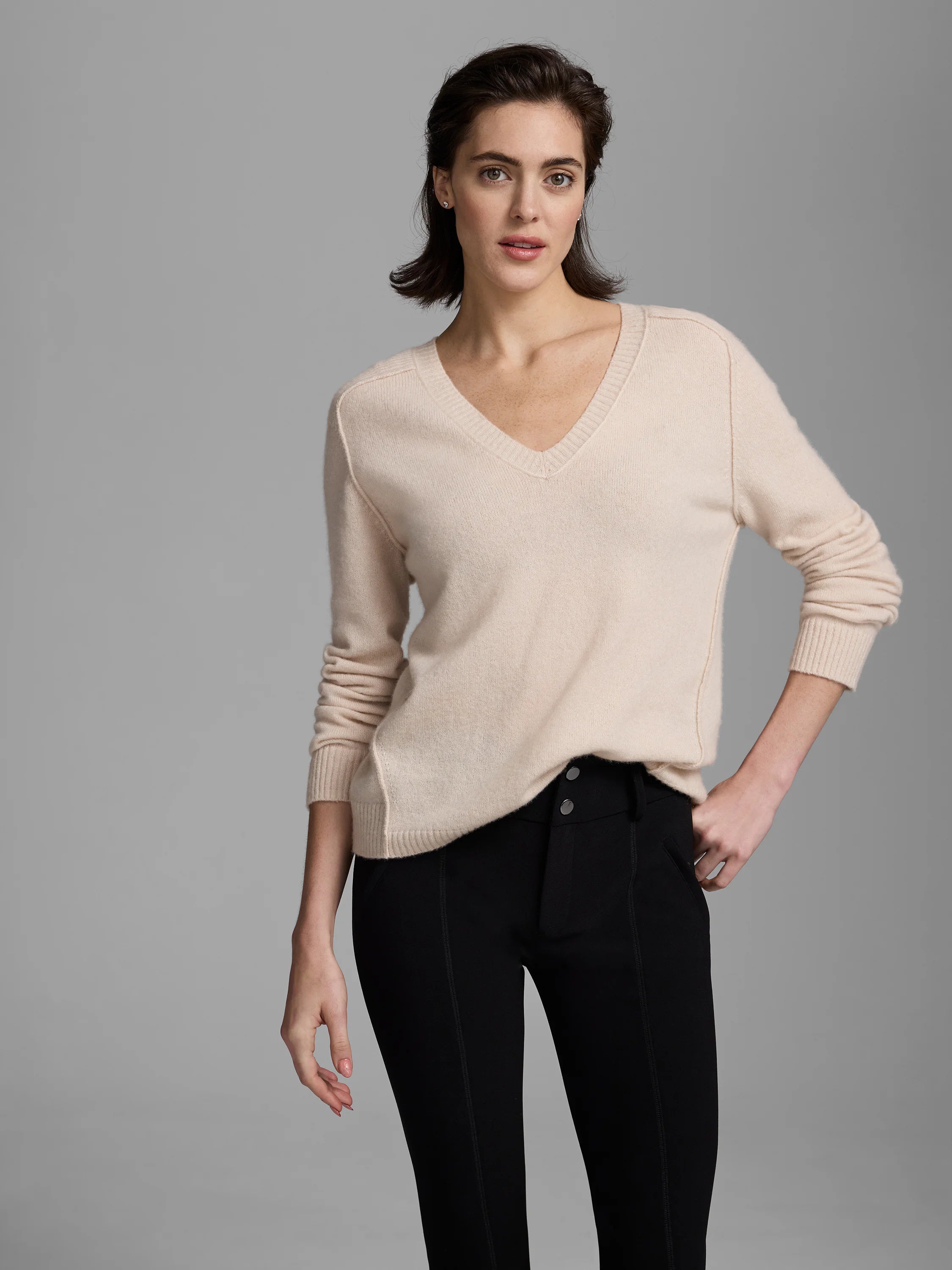 Light beige V-neck sweater with long sleeves, ribbed cuffs and hem. Shows a relaxed fit on a model.