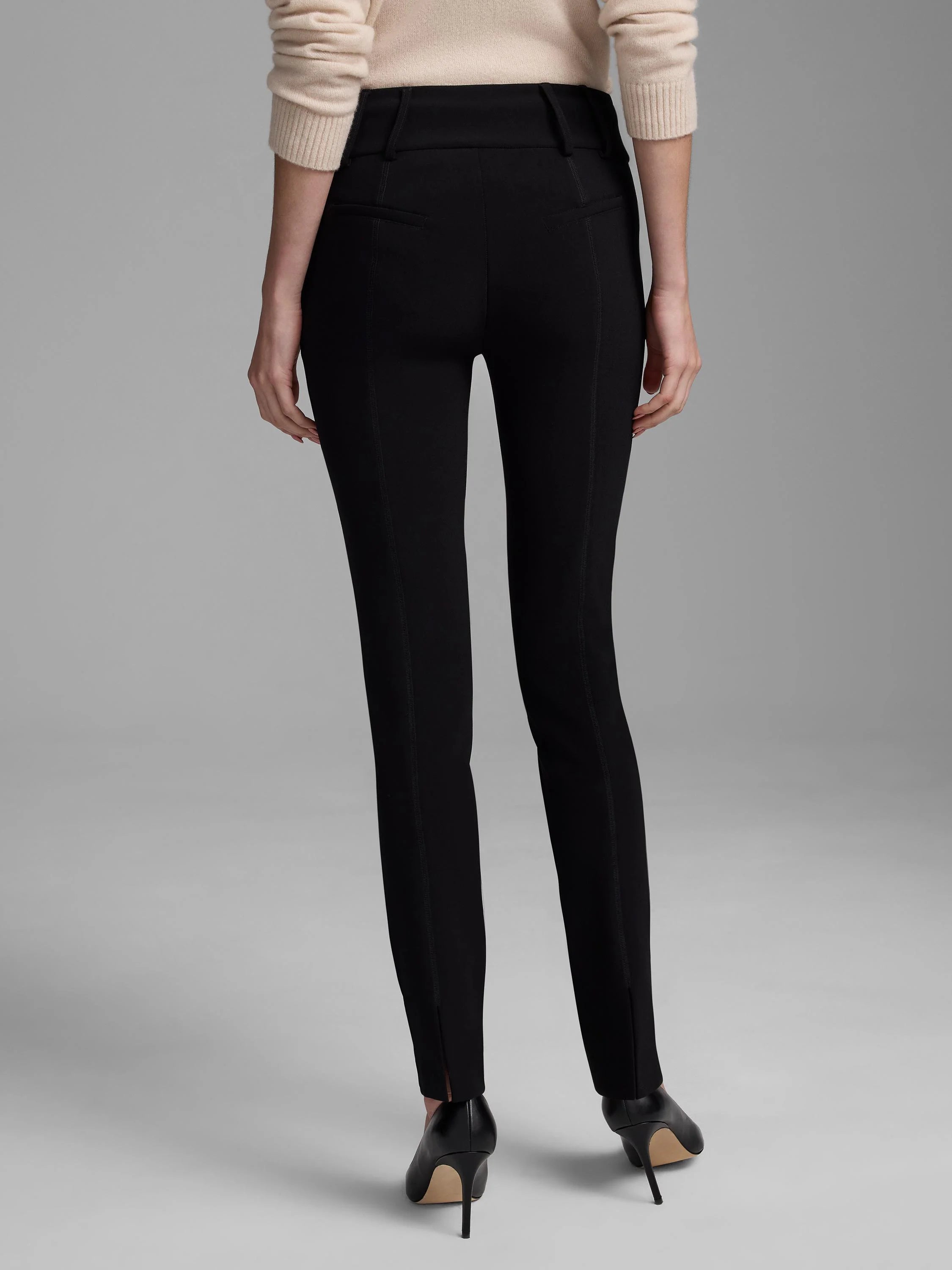 Black knit scuba slim pants, rear view. Features vertical leg seams, waistband details, and small ankle slits.