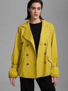 Golden yellow twill trench coat. Short, double-breasted with wide lapels, dark buttons, and elasticized cuffs.